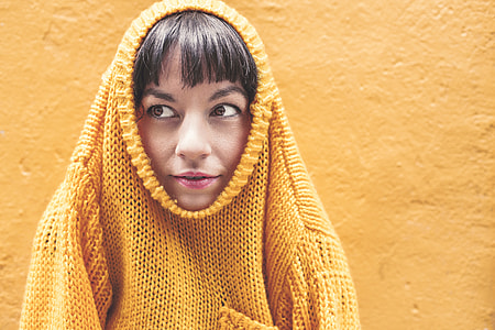 women wearing yellow knitted shirt leaning on yellow wall thumbnail