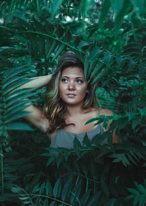 woman standing between green leaf plants thumbnail