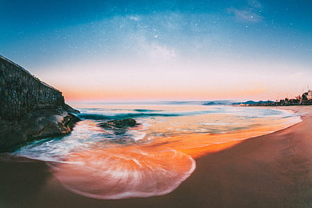 beach, body of water, and rock formation during sunset thumbnail