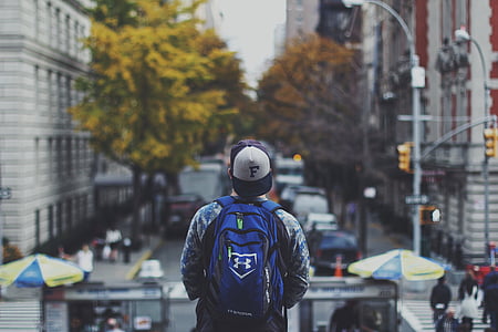 man standing near road between trees and buildings thumbnail