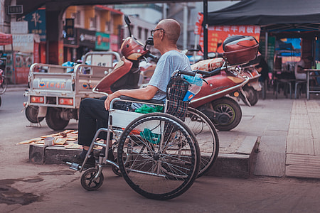 man wearing blue shirt with black pants sitting on the wheelchair near the street during day time thumbnail