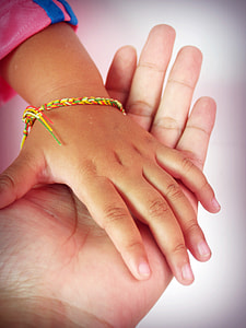 tilt lens photography of child's hand with bracelet over left palm of person thumbnail