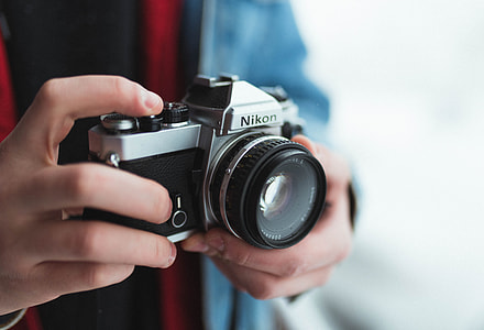 shallow focus photography of man holding Nikon SLR camera thumbnail