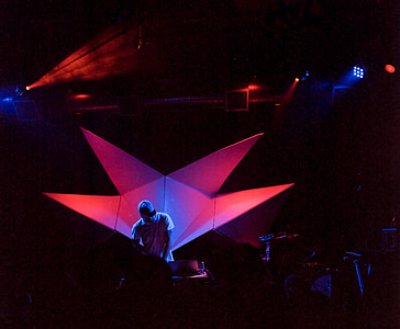 man wearing white t-shirt on stage with blue and red lights thumbnail