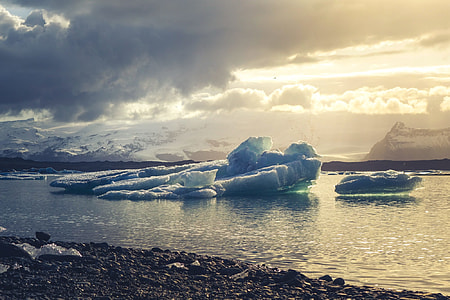 iceberg floating on calm body of water under clouded sky at daytime thumbnail