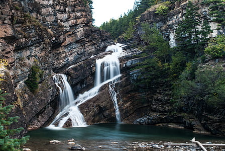 waterfalls near cliff and tree under clear sky thumbnail