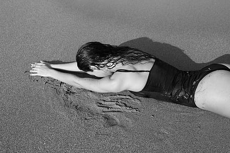 grayscale photo of woman lying on sand thumbnail