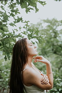 close-up photography of woman closing both eyes front of green tree thumbnail