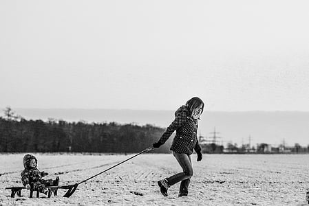 grayscale photography of woman pulling toddler riding sled thumbnail