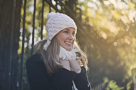 Photography of Woman in Black Jacket and White Knit Cap Smiling Next to Black Metal Fence thumbnail