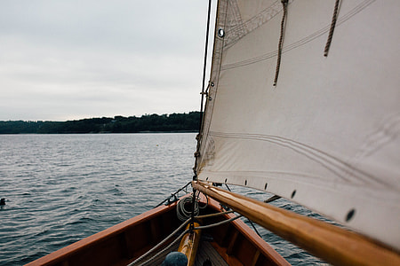 brown sailboat on ocean over silhouette of mountain under cloudy sky at daytime thumbnail