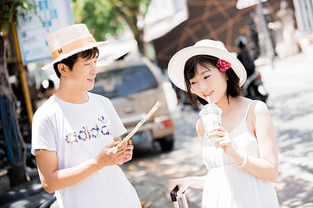 man holding hand fan beside woman wearing hat thumbnail