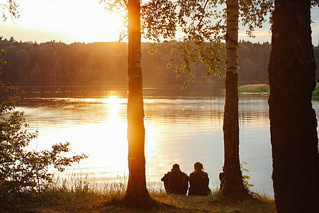 two persons sitting near body of water thumbnail