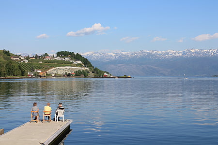 three persons sitting on chair on top of wooden dock fronting body of water thumbnail