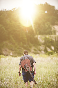 man walking on green grass carrying guitar thumbnail
