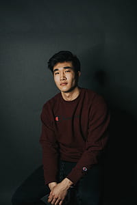 man wearing maroon Champion sweatshirt and black pants sitting while holding his both hands thumbnail