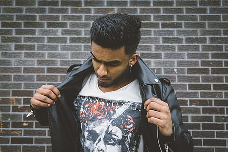 man holding his leather jacket standing near wall during daytime thumbnail