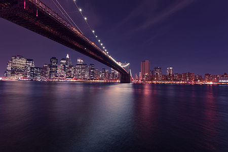 lighted suspension bridge near city buildings during nighttime thumbnail