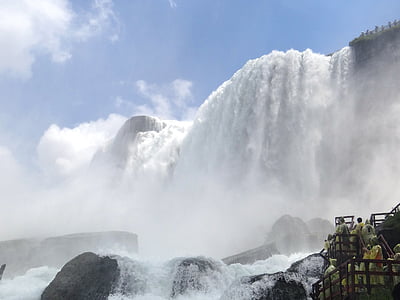 people standing on bridge facing large waterfalls during daytime thumbnail