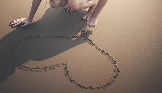 person drawing heart shape on sand thumbnail