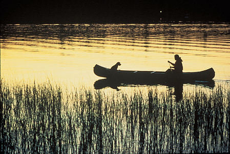 silhouette of woman and dog in canoe on body of water thumbnail