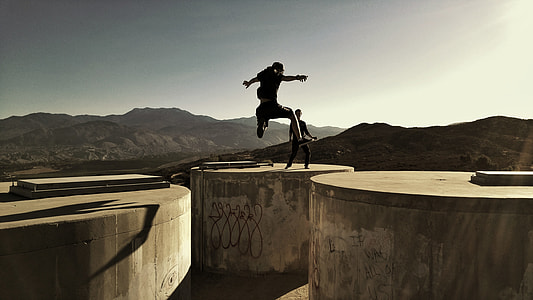 silhouette photo of man jumping between concrete container at daytime thumbnail
