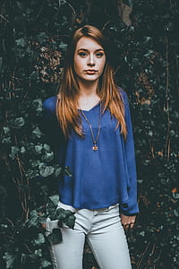 woman wearing blue long-sleeved top and white denim jeans standing near green plant thumbnail