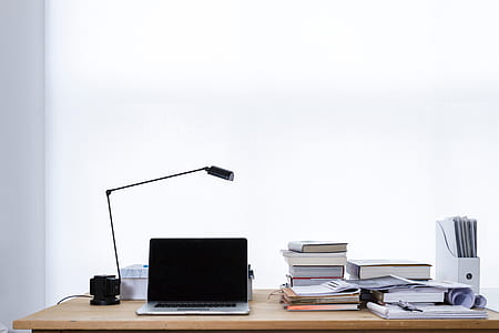 MacBook Pro beside pile of assorted-color labeled books on brown wooden desk thumbnail