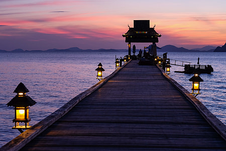 brown wooden dock with lanterns in middle of body of water thumbnail