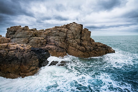 aerial photo of brown rock formation near body of water under cloudy sky during daytime thumbnail