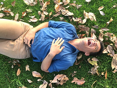 laughing man wearing blue dress shirt lying on green grass lawn thumbnail