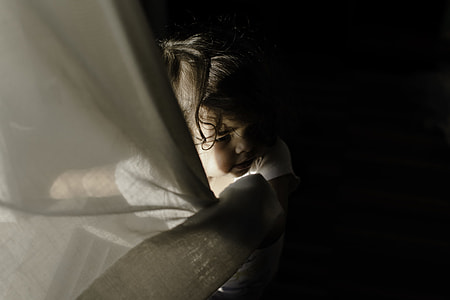 girl wearing white shirt holding curtain while standing thumbnail