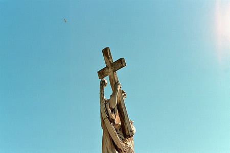 worm's eye view of man holding cross statue during daytime thumbnail