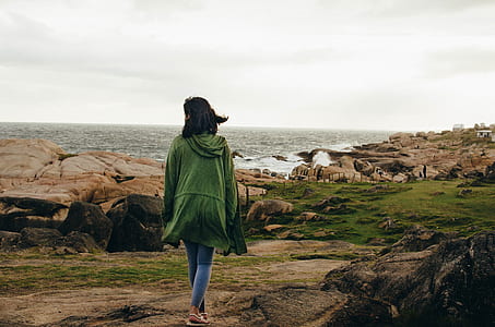 woman in green cardigan and blue denim jeans walking beside sea thumbnail