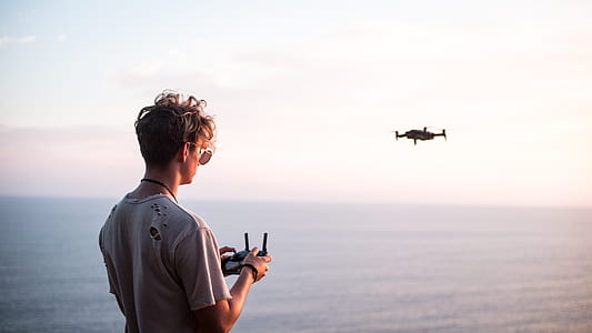 man controlling quadcopter drone above the sea during daytime thumbnail