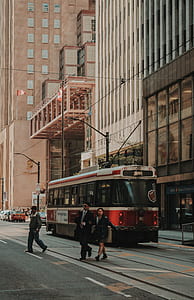 couple and man crossing street near red-and-white tram running on road near concrete building at daytime thumbnail