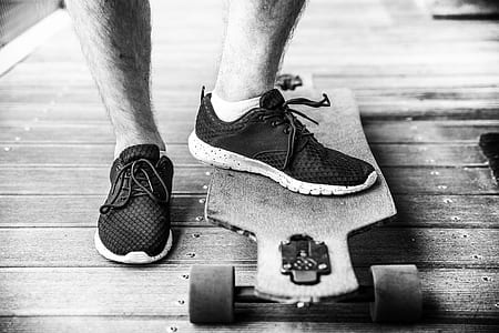 man wearing black sneakers stepping on brown longboard thumbnail