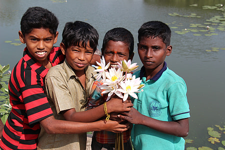 four boys holding a bouquet of white lotus flowers by body of water during daytime thumbnail