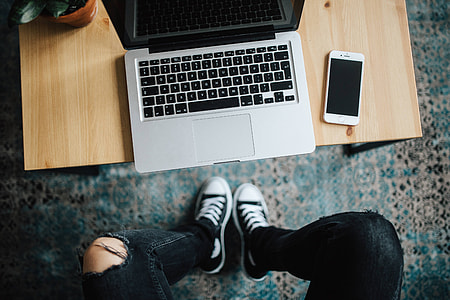 Woman in ripped jeans and black sneakers with a silver laptop on a wooden table thumbnail