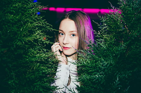woman looking sideways while right hand touching her face standing between Christmas trees thumbnail