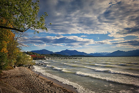 white sand near body of water and mountain under blue and white sky during daytime thumbnail