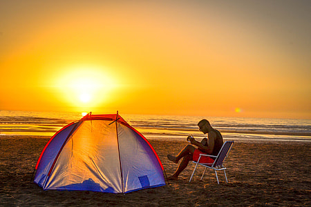 man sitting on chair playing guitar  near tent on beach shore during sunset thumbnail