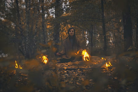 woman wearing brown cardigan sitting in forest surrounded with fireballs thumbnail