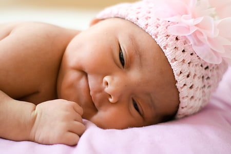 baby wearing pink knitted headband with flower accent lying on pink textile thumbnail