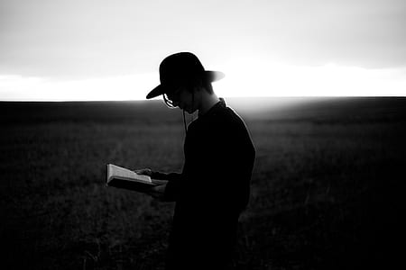 grayscale photography of a person in black dress shirt wearing black hat reading a book thumbnail