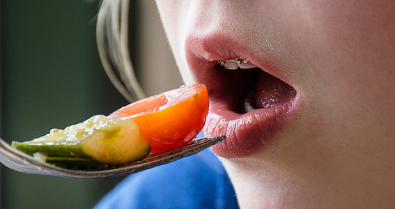 person holding fork with vegetable near mouth thumbnail