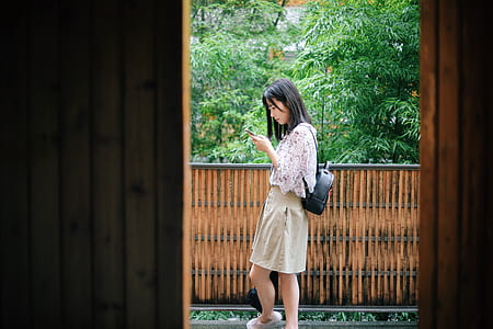 woman using smartphone beside wall and trees during daytime thumbnail