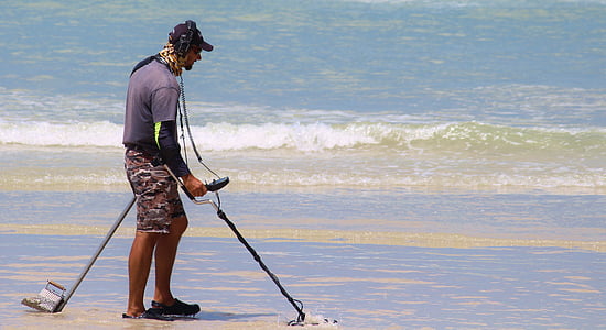 man walking on seashore while using metal detector thumbnail