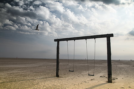 black wooden framed two wooden swing on seashore under white clouds thumbnail