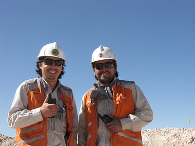 two men standing on sand with white hard helmets thumbnail